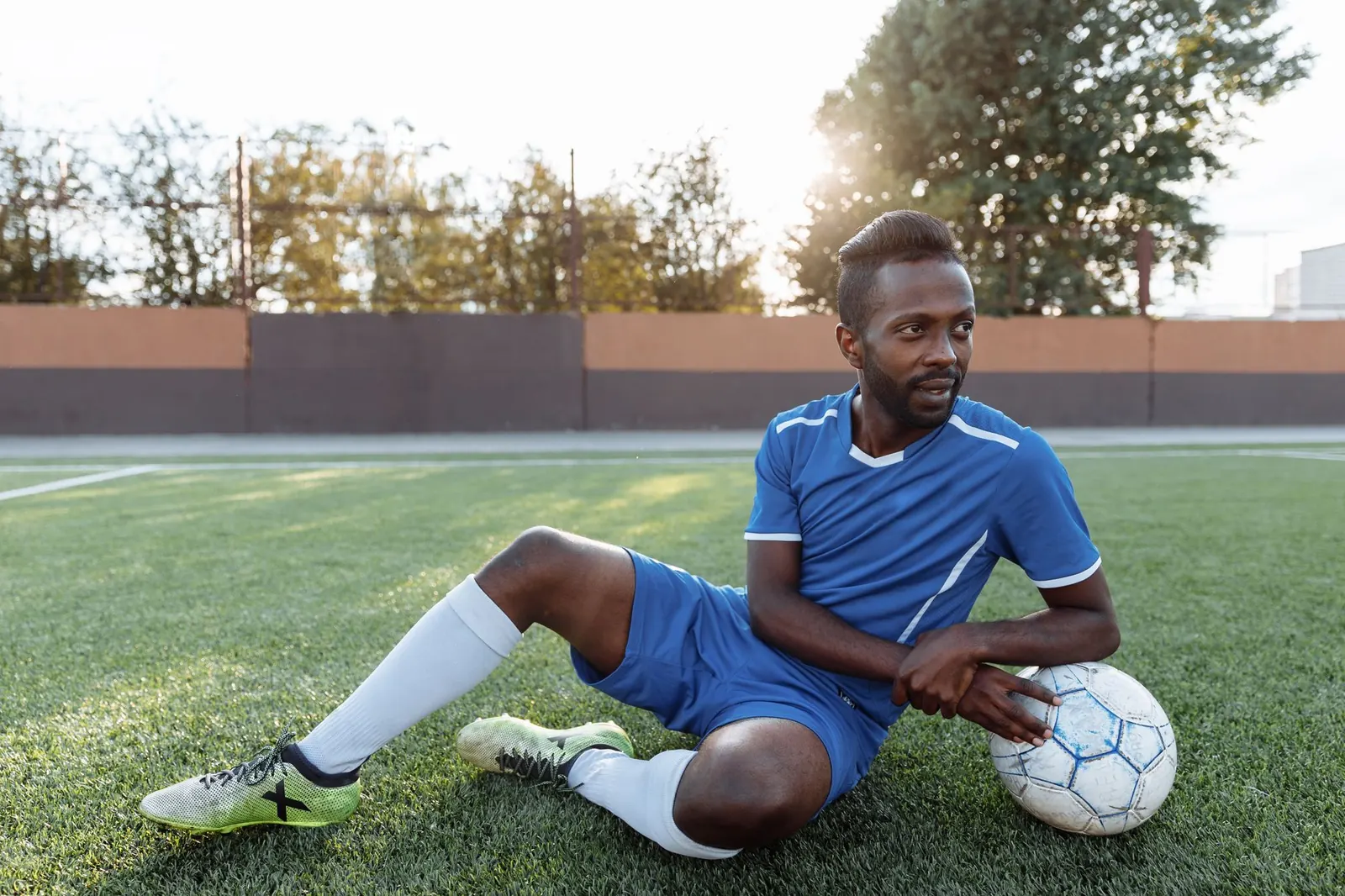 Footballer in a blue kit resting on the pitch beside a ball